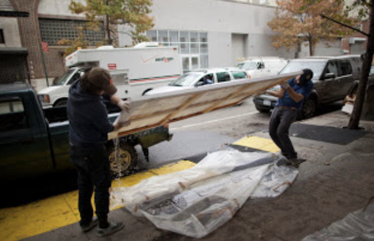 Two people move a large canvas outside.